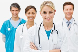 b8 Beautiful young doctor standing with hands folded and assistant doctors in background